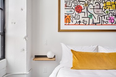 Modern loft bedroom with white bedding, yellow pillow, shelf nightstand, white globe lamp, painting